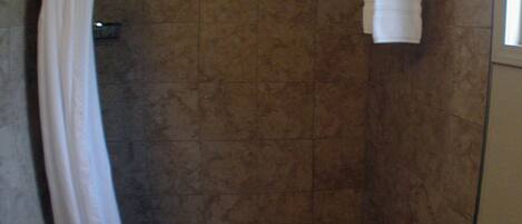 A small, enclosed shower area with a shower curtain, a towel hanging on the wall, and a ceiling light.