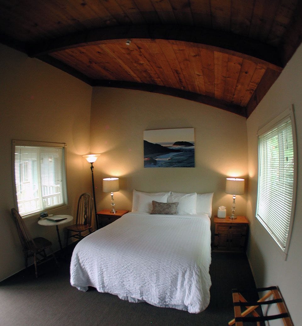 A bedroom with a large bed, two bedside lamps, a painting on the wall, and a window with blinds.