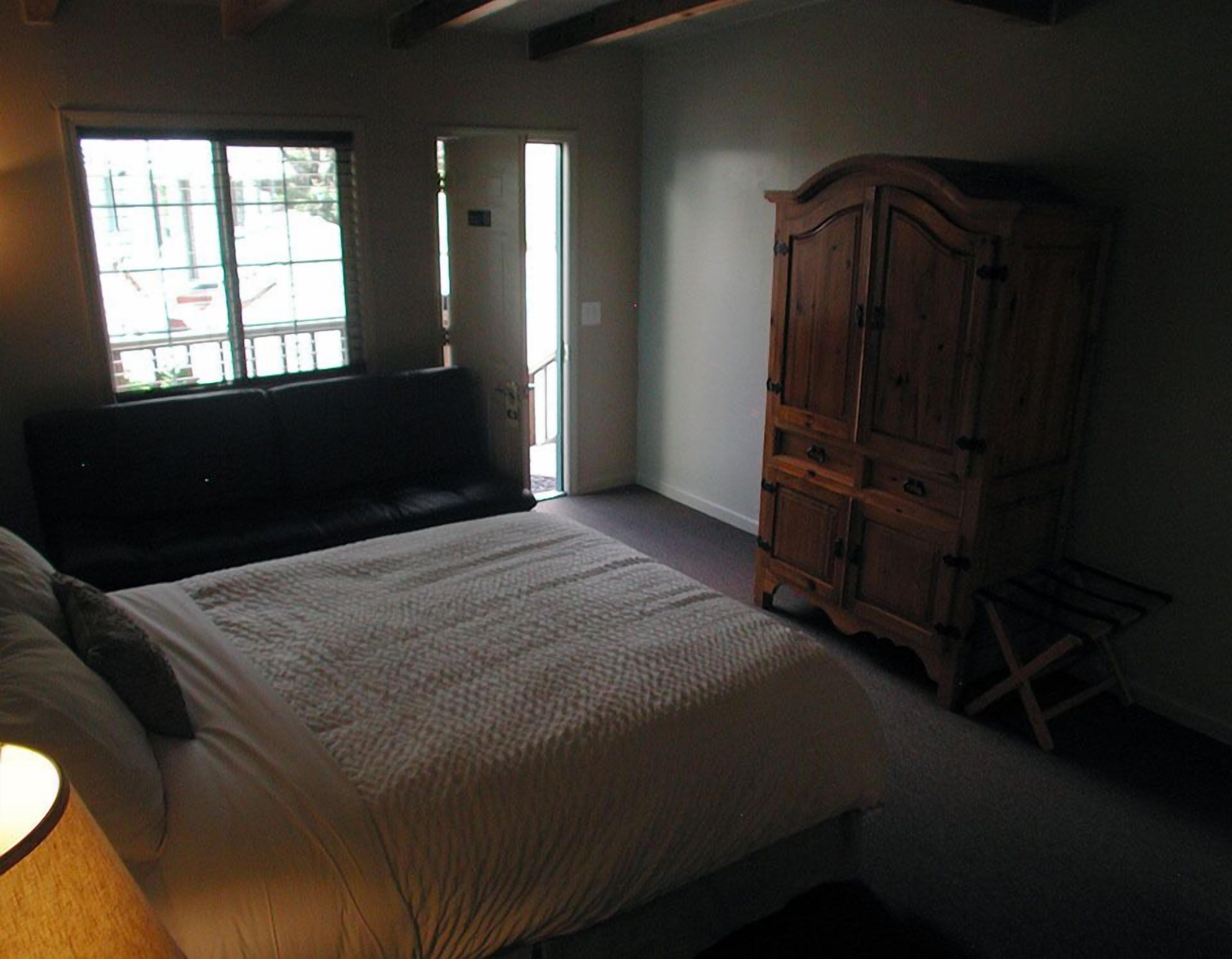 Um quarto com uma cama grande, um guarda-roupa de madeira e um banquinho.