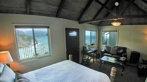 A bedroom with a large bed, a desk, a chair, and a view of the ocean. - Lucia Lodge (Big Sur)