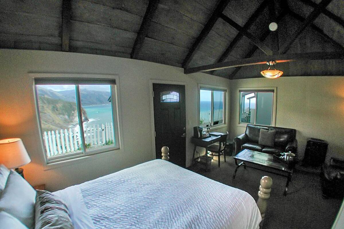 A bedroom with a large bed, a desk, a chair, and a view of the ocean.