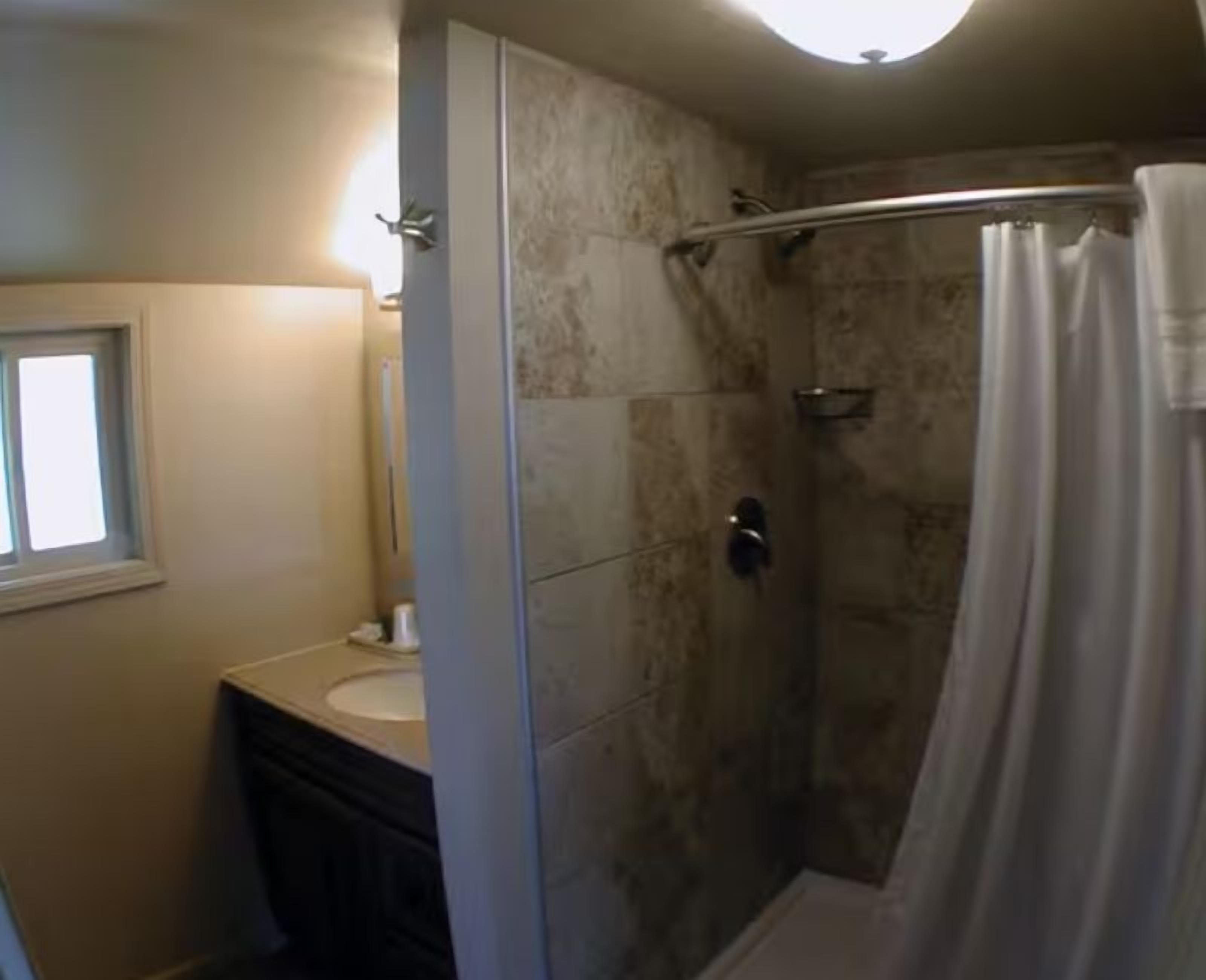 A bathroom with a shower, a sink, and a window.