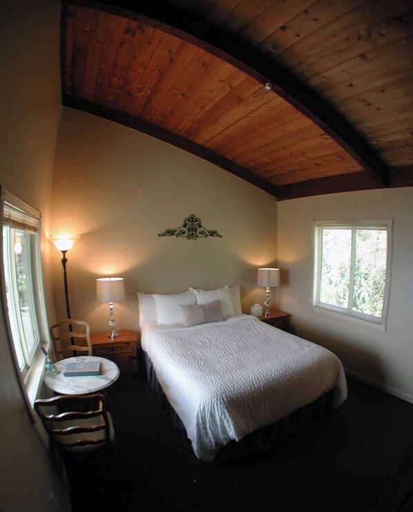 A bedroom with a bed, two bedside lamps, a small round table with a chair, and a window. - Lucia Lodge (Big Sur)