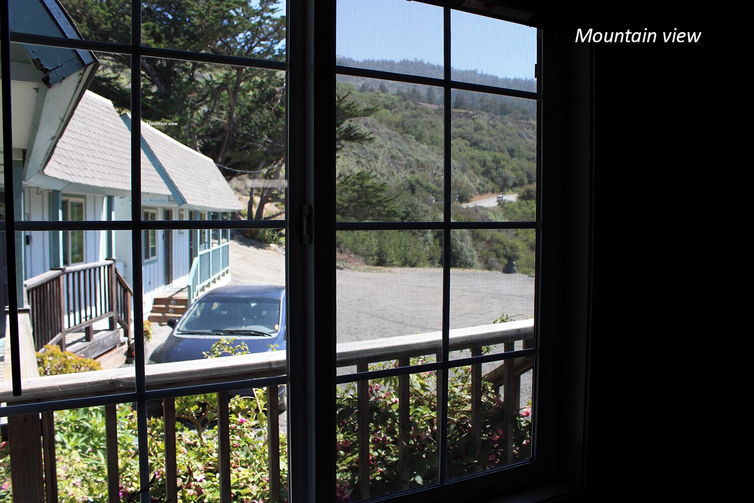 A window with a view of a house and a mountain.