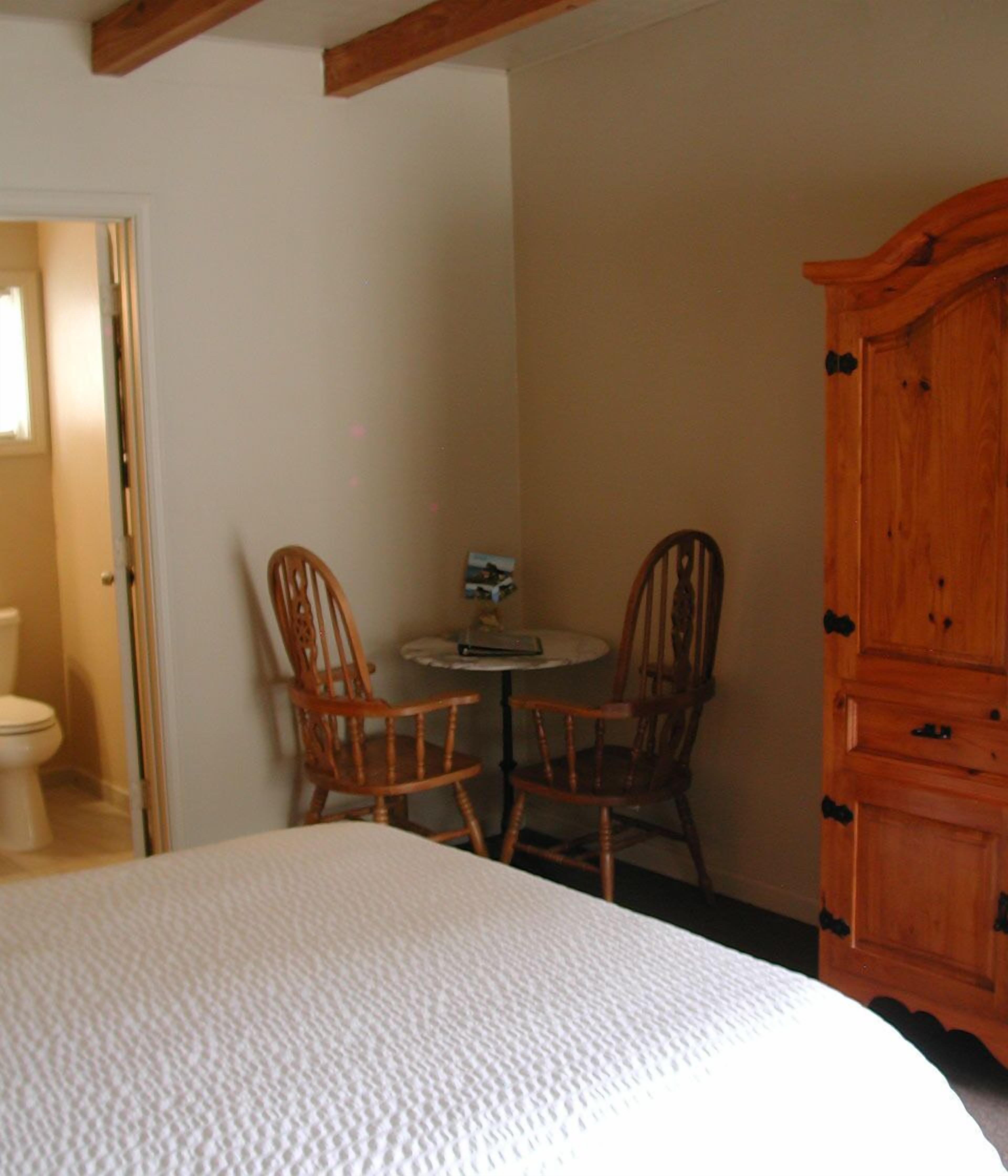 Une chambre à coucher comprenant un lit, deux chaises en bois, une petite table ronde et une armoire en bois.