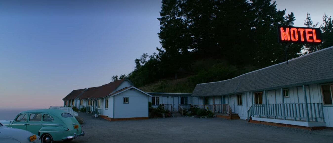 A motel with a row of single-story buildings, a parking area, and a car parked in front.