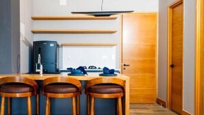 Een kleine keuken met een centraal eiland, barkrukken, een koelkast en een houten deur.