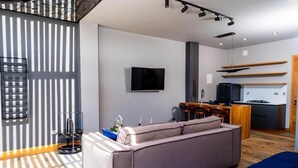 Een moderne woonkamer met een bank, een flatscreen televisie en een keukenhoek met een eettafel en stoelen.