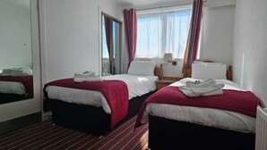 Une chambre d’hôtel avec deux lits simples, un miroir, une fenêtre avec des rideaux et un radiateur.