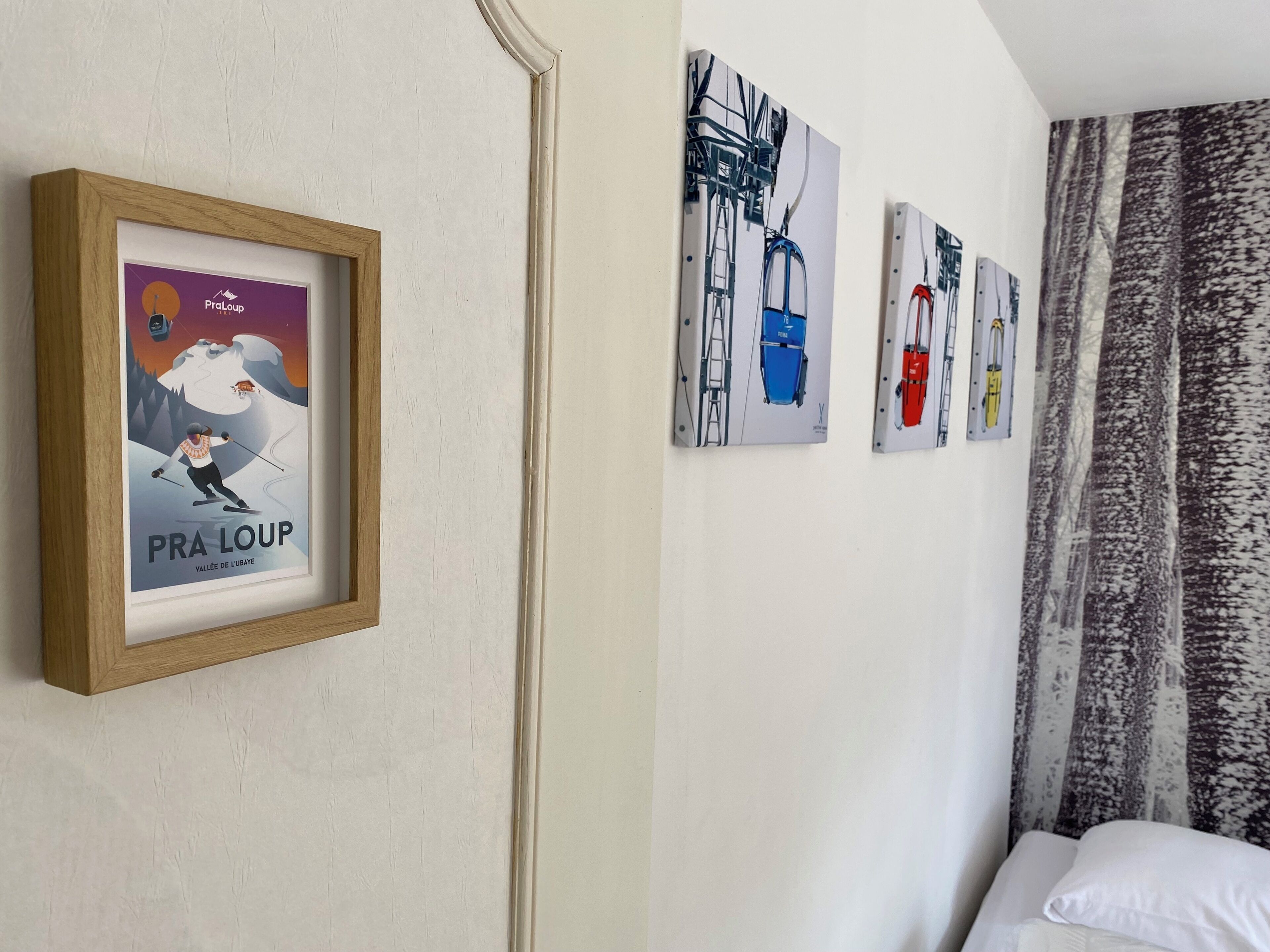 A hotel room with a bed, a framed poster of a ski scene, and three wall-mounted artworks depicting ski lifts.