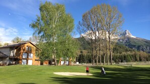 Un terrain de golf avec une maison en arrière-plan et des montagnes au loin.