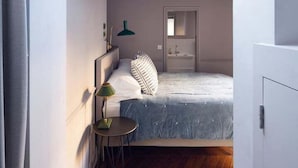 A narrow hallway leading to a bedroom with a bed, a bedside table, and a lamp.