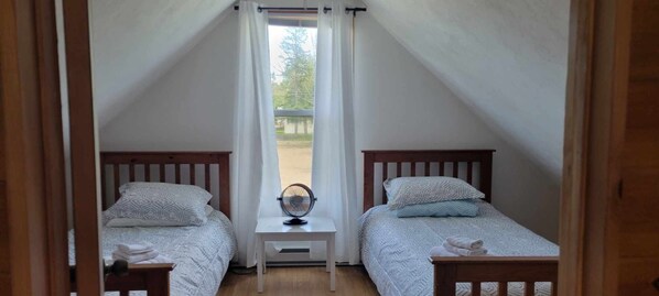 Une chambre avec deux lits, chacun doté d’une tête de lit en bois, d’une petite table de chevet et d’un ventilateur.