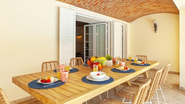 A wooden dining table with a fruit bowl, plates, and glasses, set in a room with a brick ceiling and white walls. - Villa with heatable pool and BBQ in Albufeira (Albufeira)
