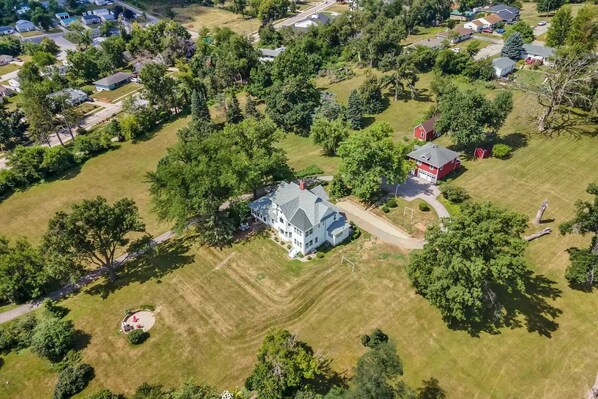 An aerial view of a residential area with a large white house surrounded by trees and open grassy areas.