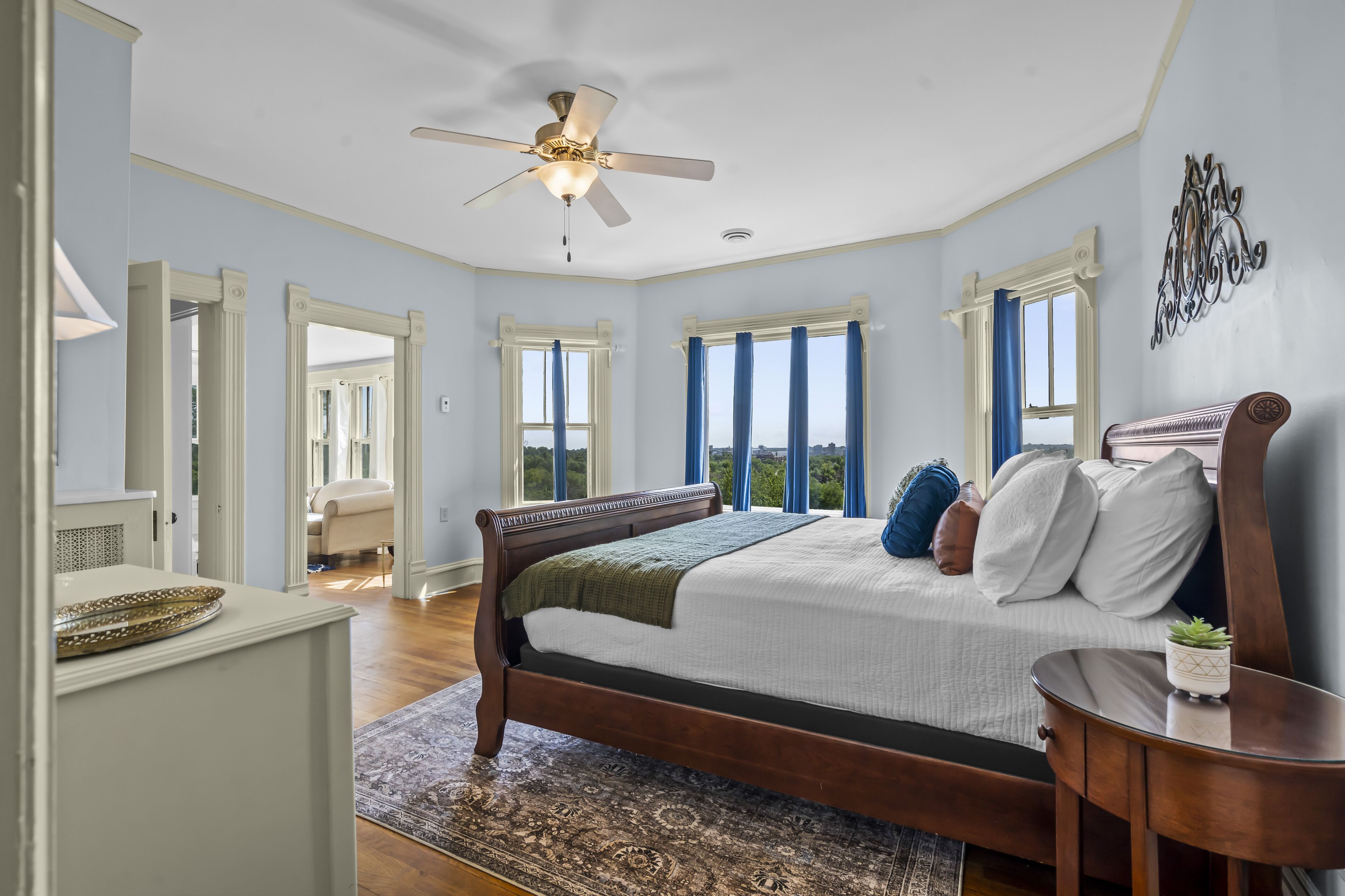 Une chambre avec un grand lit, un ventilateur de plafond et plusieurs fenêtres équipées de rideaux.