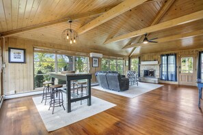 A spacious room with wooden floors, a dining area with stools, a sofa, and a fireplace.