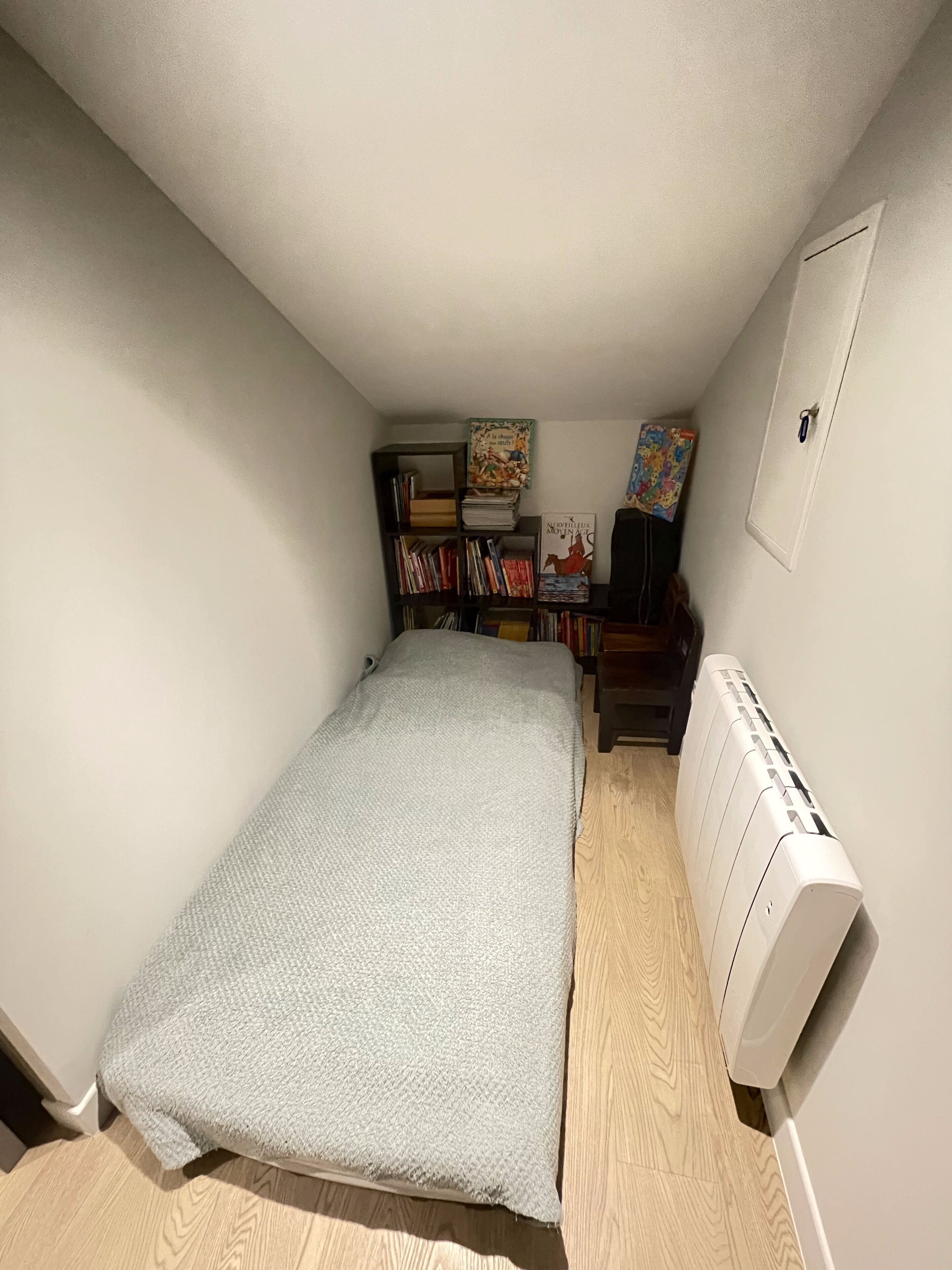 A small, neatly arranged bedroom with a single bed, a bookshelf, and a radiator.