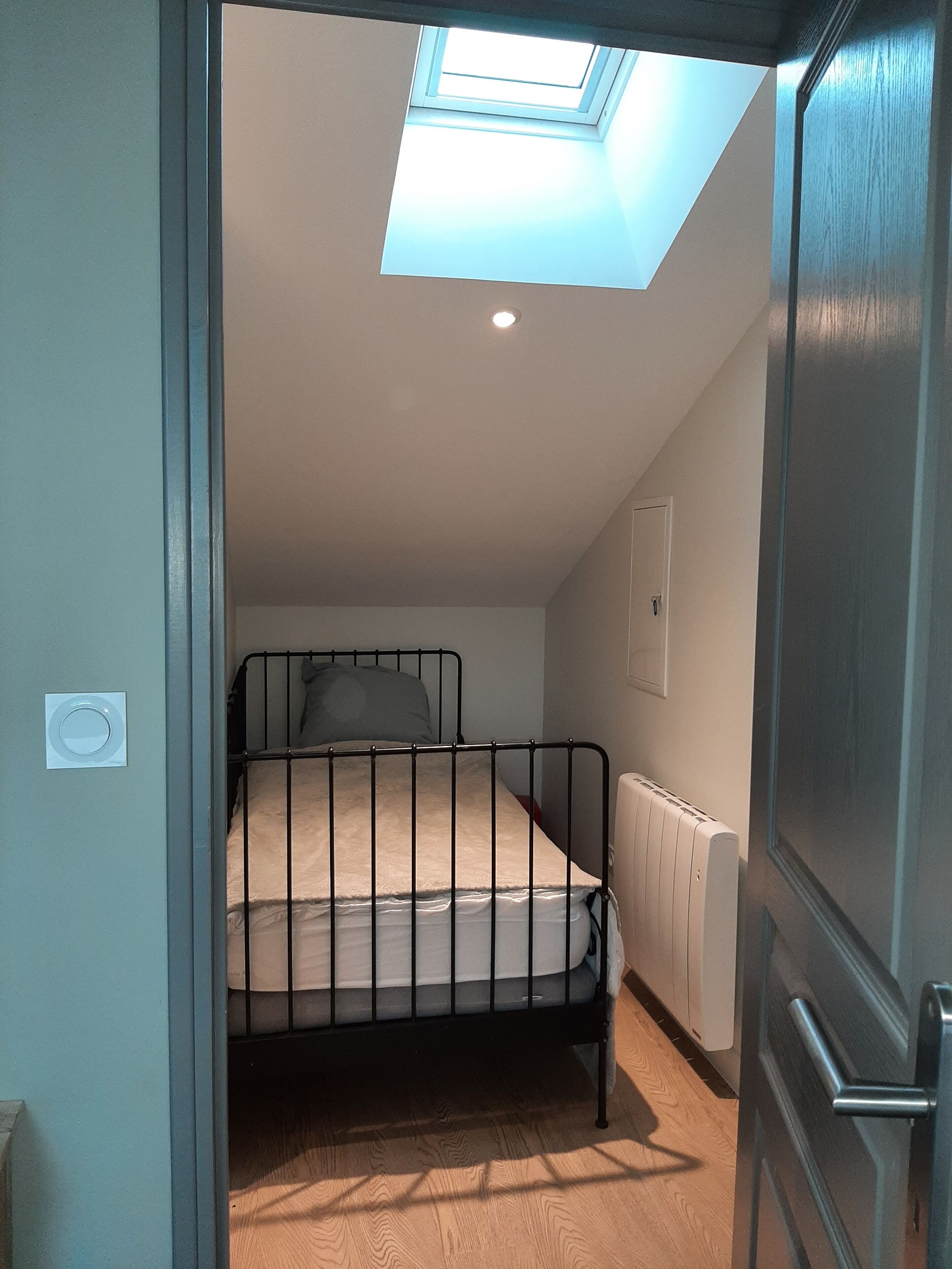 Un dormitorio pequeño con un tragaluz, una cama individual, un radiador y una puerta.