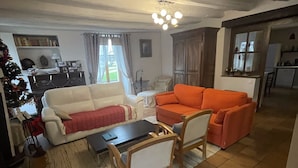 Un salon avec un canapé blanc, un canapé orange, une table basse en bois et un tapis. Un sapin de Noël se trouve dans un coin.