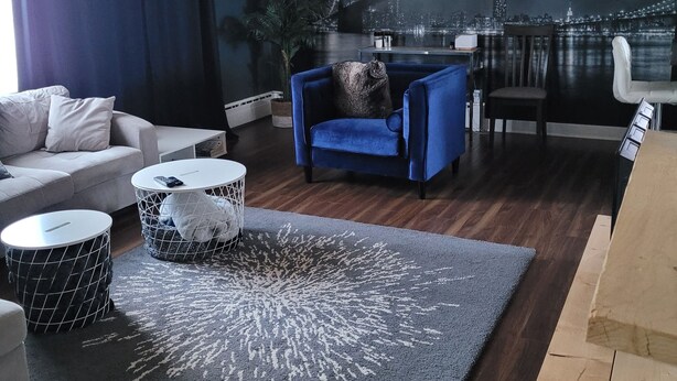 Een moderne woonkamer met een stadsgezicht muurschildering, een bank, een blauwe fauteuil en een ronde salontafel.
