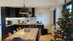 Une cuisine moderne avec des meubles de couleur sombre, une grande table à manger et un sapin de Noël décoré d’ornements rouges.