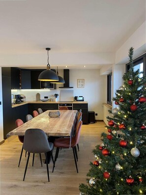 Uma cozinha moderna com armários escuros, uma grande mesa de jantar e um pinheiro de Natal decorado com enfeites vermelhos.