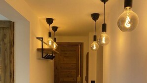 Un couloir au sol en bois, une porte en bois au fond, et des suspensions avec des ampoules apparentes.