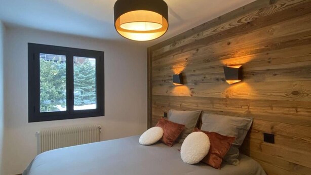 Une chambre avec un grand lit, une fenêtre, un mur en bois et un luminaire au plafond.