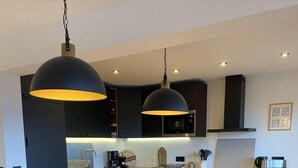 Une cuisine moderne avec une table à manger en bois, des meubles de rangement noirs et des luminaires suspendus.