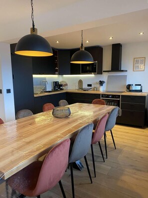 Cozinha moderna com mesa de jantar de madeira, armários pretos e iluminação pendente.