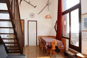 A dining area with a table set for four, wooden chairs, a clock on the wall, and a window with curtains.