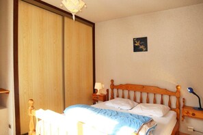 A bedroom with a wooden bed, a nightstand, a bedside lamp, a wall-mounted artwork, and a sliding door.