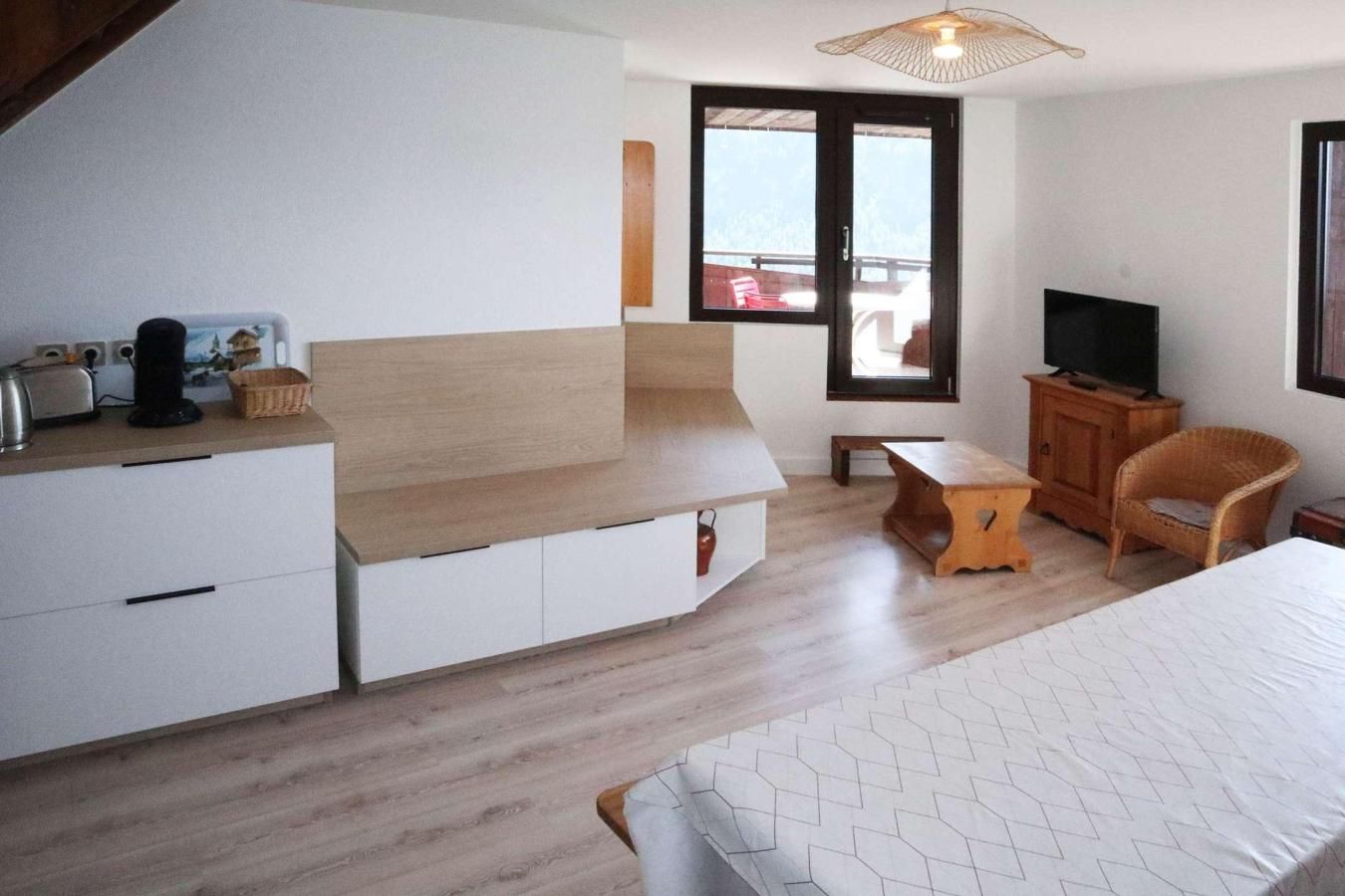 A modern bedroom with a bed, a TV, a wooden bench, and a balcony view.