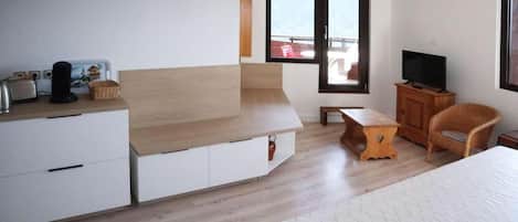 Ein modernes Schlafzimmer mit einem Bett, einem Fernseher, einer Holzbank und Balkonblick.