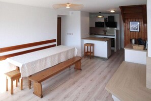 A compact room with a bed, a bench, a small stool, and a kitchenette.