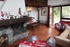 Un salon chaleureux avec une cheminée en pierre, des meubles en bois et une grande fenêtre donnant sur l’extérieur.