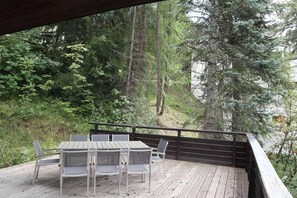 Une terrasse extérieure avec une table et des chaises, entourée d’une forêt dense et de grands arbres.
