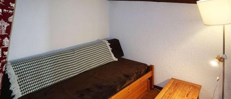 A small, cozy room with a single bed, a wooden nightstand, a lamp, and a framed picture on the wall.