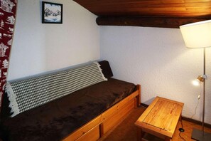 Une petite chambre accueillante, avec un lit simple, une table de chevet en bois, une lampe et un tableau encadré au mur.