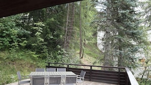 An outdoor deck with a table and chairs, surrounded by dense forest and tall trees. - Chalet, 200m from shops, view valley, terrace, fireplace or stove, tv, 100m², Les Orres (Les Orres)