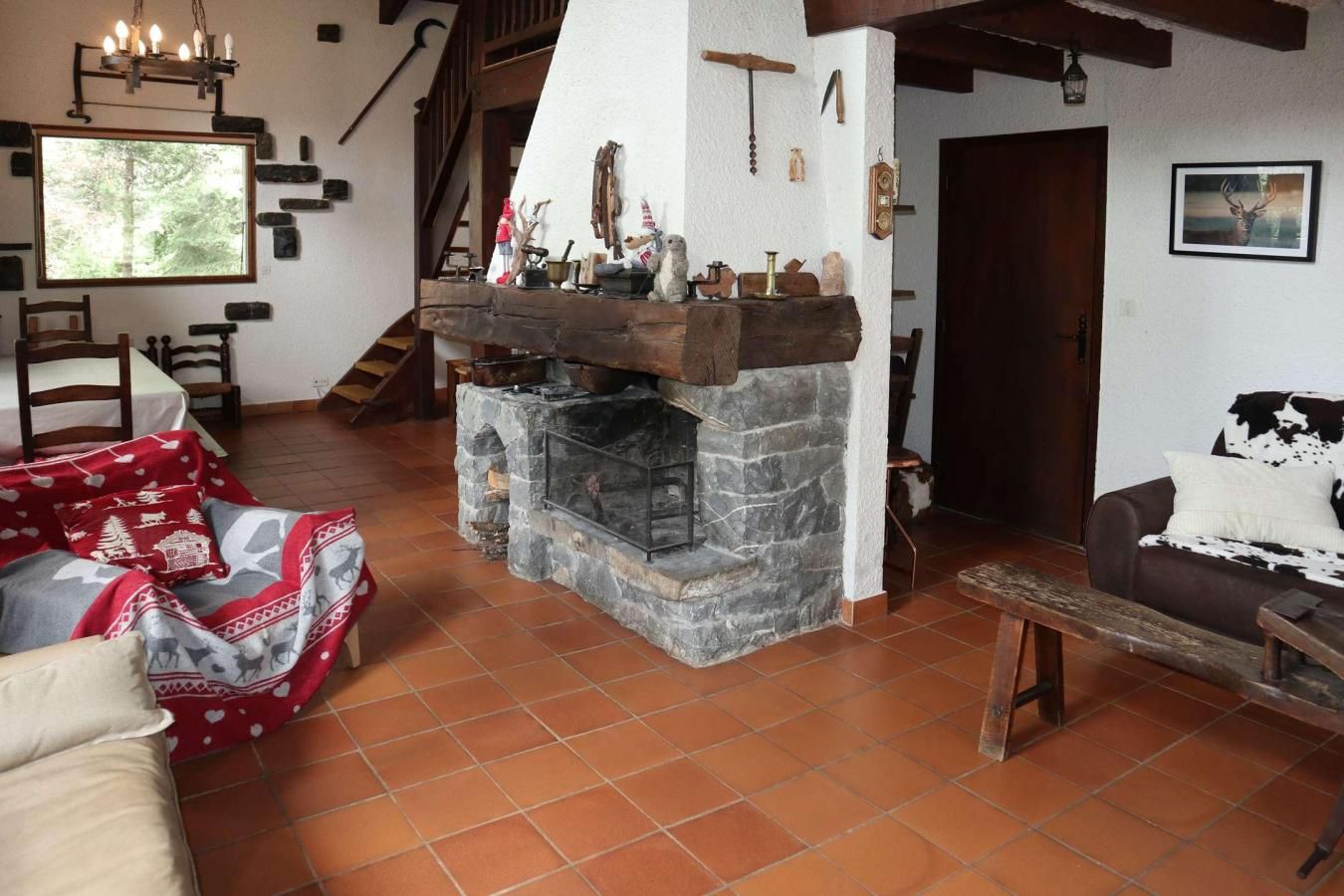 A cozy living room with a stone fireplace, a wooden staircase, and rustic decor.
