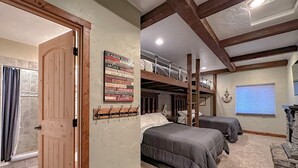 Une chambre de style cabane avec des lits superposés, une porte en bois, un tableau d’affichage où sont accrochées diverses notes et une cheminée en pierre.