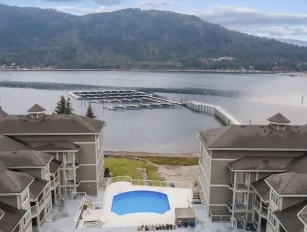 A hotel with a swimming pool, a dock, and a view of a lake and mountains.