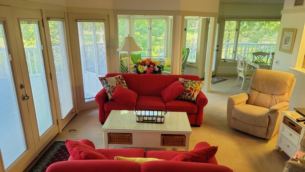 A living room with a red sofa, beige armchair, and a glass coffee table. - Wonderful Oasis in Kingston Plantation, near the Embassy and Hilton.  (Myrtle Beach)