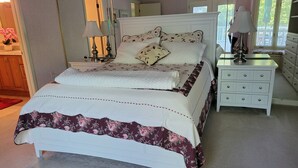A neatly made bed with floral bedding, a white nightstand with drawers, and a mirror above the bed. - Wonderful Oasis in Kingston Plantation, near the Embassy and Hilton.  (Myrtle Beach)