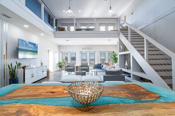 A spacious living area with a large wooden coffee table, a woven basket, and a view of the ocean through large windows.
