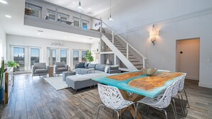 A spacious living area with a high ceiling, a staircase, and a dining table with chairs.
