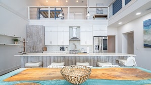 A modern kitchen with white cabinets, a central island, and a dining area with a wooden table and chairs.