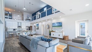A spacious living area with a large gray sectional sofa, a wooden coffee table, and a dining area with a white table and chairs.